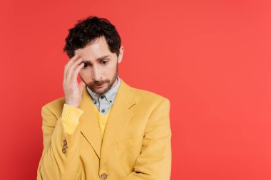nervous man in yellow blazer touching forehead while looking down isolated on pink coral  clipart