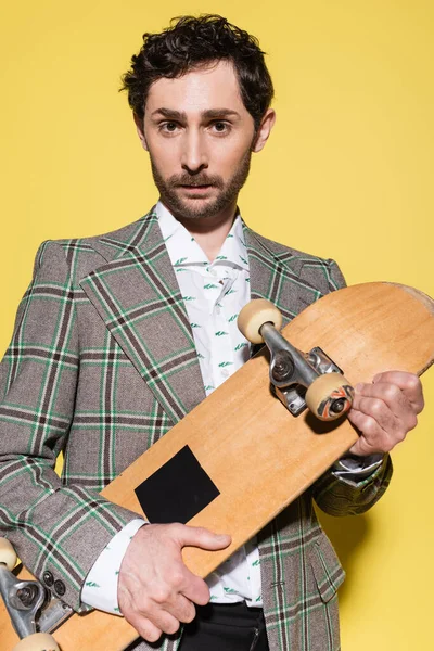 魅力的な男保持スケートの肖像と見てカメラで黄色の背景 — ストック写真