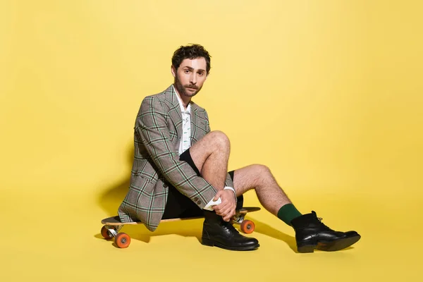 Stijlvolle Man Blazer Short Zittend Skateboard Gele Achtergrond — Stockfoto