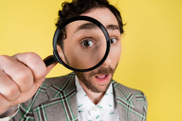 Wide angle view of stylish man looking through magnifying glass isolated on yellow  