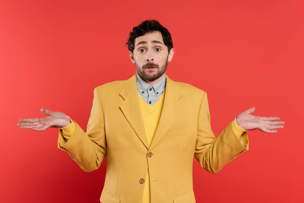 Confused man in yellow jacket showing shrug gesture on coral background