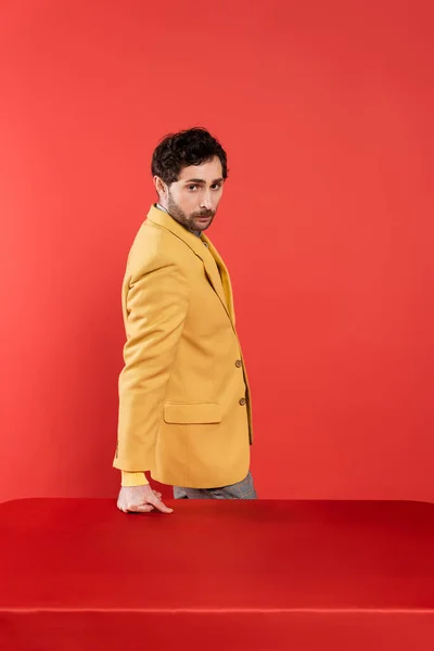 Affascinante Uomo Elegante Giacca Gialla Piedi Vicino Tavolo Rosso Guardando — Foto Stock