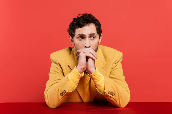 thoughtful man with clenched hands leaning on table isolated on red coral background 