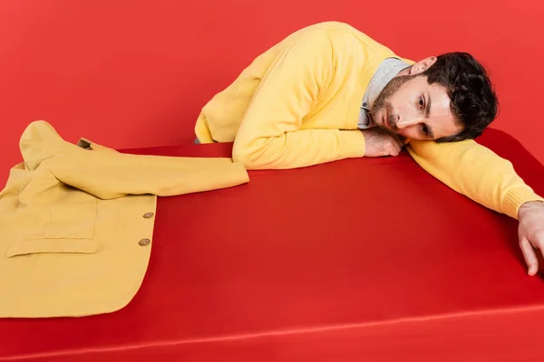 疲れた男です黄色の長袖ジャンパーサンゴの背景に隔離されたブレザーの近くの赤い机の上に横たわって — ストック写真