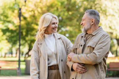 Happy blonde woman looking at husband while spending time in park  clipart
