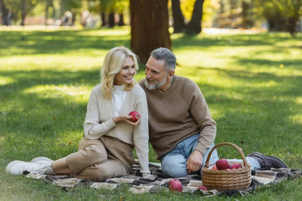 明るいです中年女性保持熟れたリンゴ近くベアドド夫の間にピクニックで公園 — ストック写真