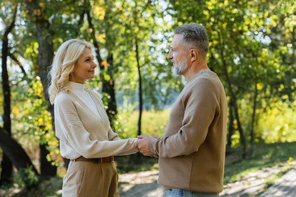 幸福的成熟夫妇手牵着手 在绿地公园里互相望着对方的侧视图 — 图库照片