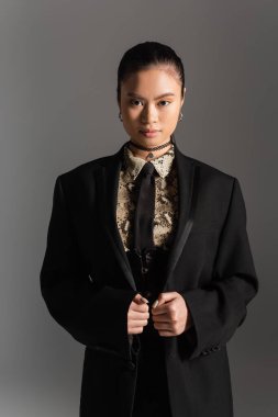 Ceketli şık Asyalı model gri renkli kameraya bakıyor. 