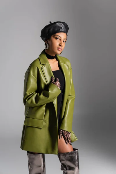 Fashionable african american model in leather beret and coat posing isolated on grey