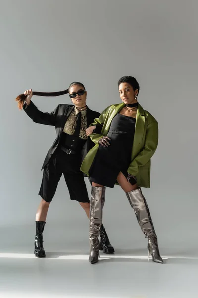 Fashionable interracial models in boots and spring clothes posing on grey background with sunlight