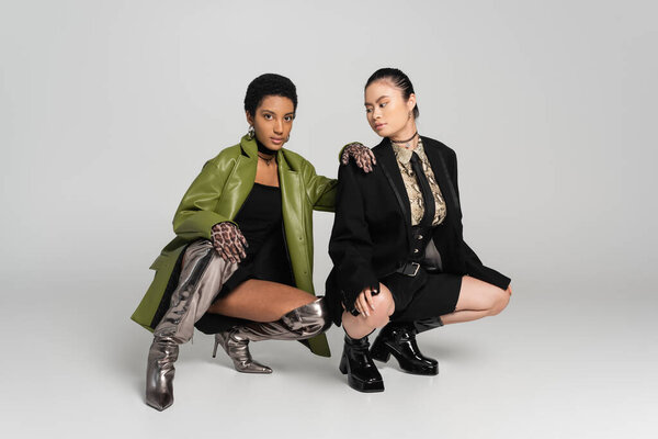 Модная африканская американка в пеньюаре позирует рядом с азиатской девушкой на сером фоне