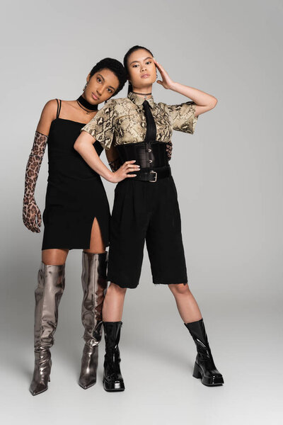Полная длина межрасовых подружек в стильных нарядах, позирующих на сером фоне