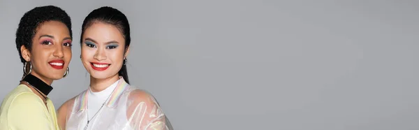 Uśmiechnięte Międzyrasowe Modelki Kolorowym Makijażem Stojące Odizolowane Szarym Banerowym — Zdjęcie stockowe