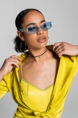 pretty african american woman in blue sunglasses and hoop earrings posing isolated on grey  clipart