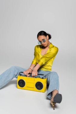 Mavili Afro-Amerikalı kadın gri üzerinde retro müzik kutusuyla poz veriyor. 