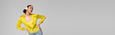 Moda Afro-Amerikan modeli kablosuz kulaklıkla müzik dinliyor ve elleri ile poz veriyor. Gri pankartta izole edilmiş kalçalar üzerinde. 