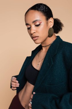 Genç Afro-Amerikan modeli. Ekin bluzlu ve büyük yün ceketli. Bej üzerine izole edilmiş poz veriyor. 