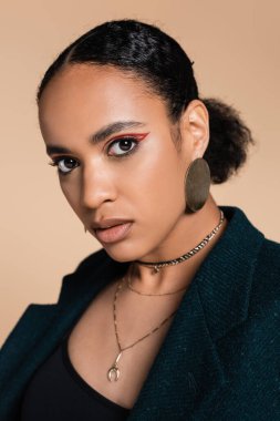 Yünlü, büyük beden ceketli, bej renkli kameraya bakan Afro-Amerikan modelinin portresi. 