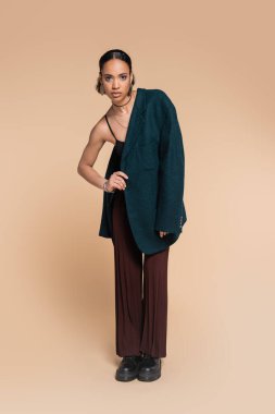 Omzunda büyük beden ceketi olan, elleri bej rengi kalçasında poz veren Afro-Amerikan model. 