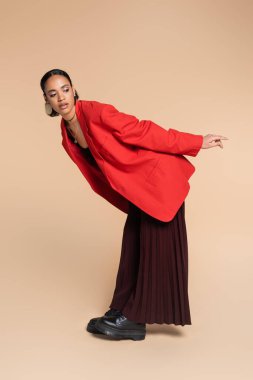 Afro-Amerikan modeli, geniş pantolonlu ve bej renkli parlak kırmızı ceketli. 