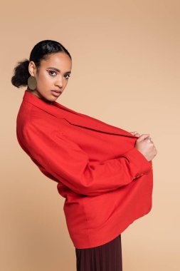 Şık Afro-Amerikan modeli bej rengi ceketle poz verirken kırmızı ceketi ayarlıyor. 