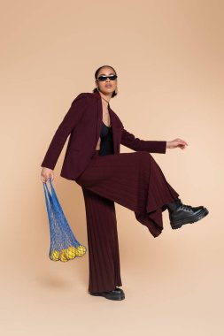 Bordo takım elbiseli, güneş gözlüklü, bej üzerine limon konmuş ağlı çanta taşıyan Afro-Amerikan kadınlarıyla dolu.  