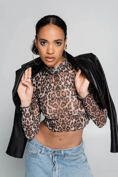 fashionable african american model in crop top with animal print wearing leather jacket isolated on grey