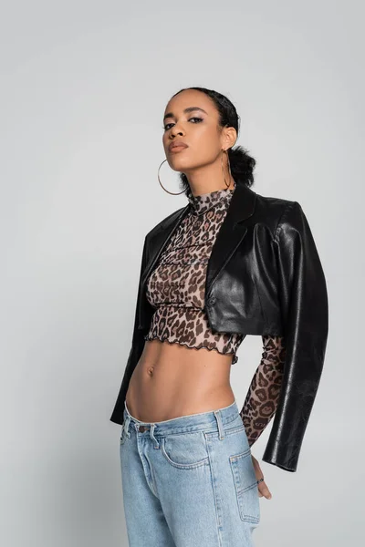 stock image stylish african american model in crop top with animal print and black leather jacket posing isolated on grey 