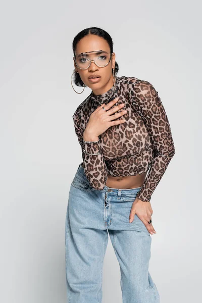 stylish african american model in crop top with animal print and trendy sunglasses posing isolated on grey