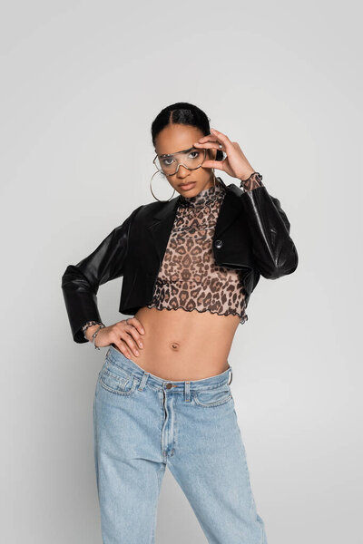 стройная африканская американка в обрезанной куртке и модных солнцезащитных очках позирует изолированно на сером 