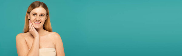 Positive young woman with freckles standing isolated on turquoise, banner 