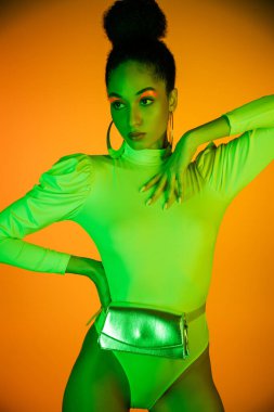 Neon giysili ve makyajlı son moda Afrikalı Amerikalı kadın turuncu arka planda poz veriyor. 