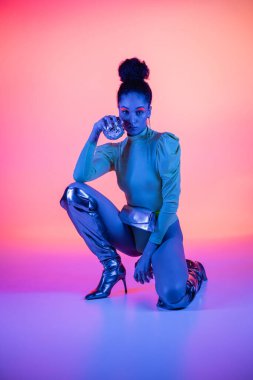 Pembe ve mor arka planda disko topları tutan neon yüzlü modaya uygun Afrikalı Amerikalı kadın.