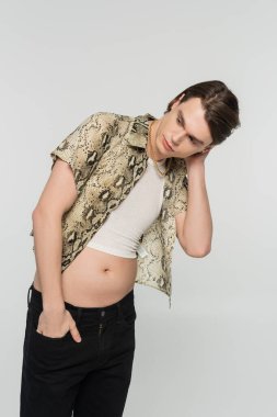 Hayvan desenli bluzuyla moda olan biseksüel model siyah pantolonun cebinde duruyor ve gri renkten soyutlanmış bir şekilde yüzünü çeviriyor.