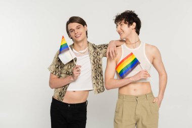 Neşeli ve şık biseksüel modeller Gri üzerinde küçük lgbt bayraklarıyla poz veriyorlar