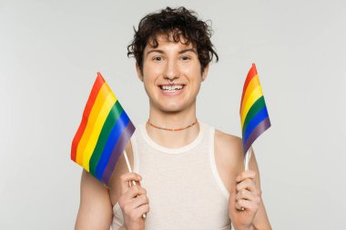 Renkli boncuklar içinde neşeli olmayan kişi gri üzerinde küçük lgbt bayrakları taşıyor.
