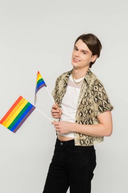 Yılan derisi bluzlu mutlu çift cinsiyetli insan gri üzerinde küçük lgbt bayrakları taşıyor.