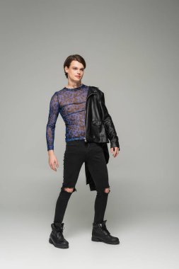 Gri arka planda siyah yırtık pantolon ve hayvan baskısı üstteki son moda çift cinsiyetli kişi.