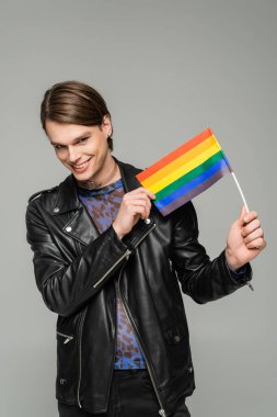 Siyah deri ceketli mutlu bir panseksüel. Gri üzerinde küçük LGBT bayrağı taşıyor.