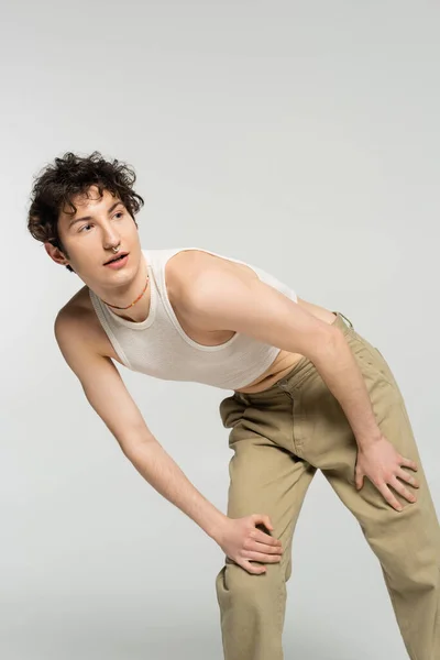 curious pansexual person in crop top and beige pants looking away isolated on grey