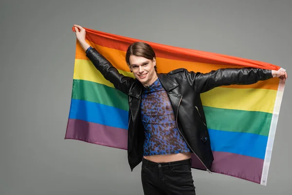 cheerful bigender person in black leather jacket posing with lgbt flag isolated on grey