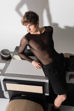 Siyah şeffaf üstteki çift cinsiyetli kişinin yüksek açılı görüntüsü gri arkaplanda fotoğraf makinesinin büyük bir modelinin üzerinde oturuyor.