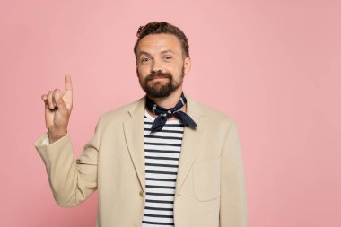 Ceket ve boyun atkısı giymiş iyi giyimli bir Fransız, pembe üzerine izole edilmiş bir şekilde kameraya bakıyor. 