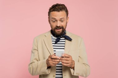 blazer ceket ve boyun atkısı giymiş heyecanlı bir Fransız. Pembe üzerine izole akıllı telefondan mesaj yolluyor. 