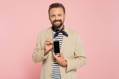 Ceketli ve atkılı mutlu bir Fransız. Elinde pembe perdeli akıllı bir telefon var. 
