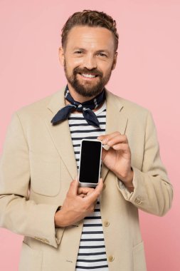 blazer ceket ve boyun atkısı takan neşeli bir Fransız. Elinde pembe ekranda boş ekranlı akıllı bir telefon tutuyor. 