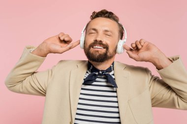 Ceketli ve boyunluklu Fransız adam pembe kulaklıklı kablosuz kulaklıkla müzik dinliyor. 