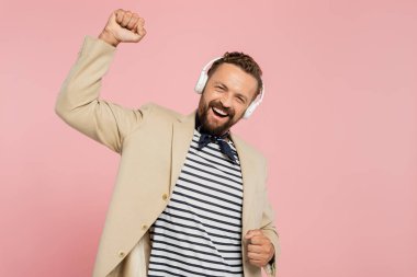 Heyecanlı bir Fransız ceketli ve boyun atkısı takmış pembe kablosuz kulaklıklarla müzik dinliyor. 