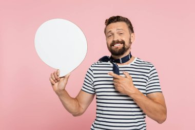 Çizgili tişört ve boyun atkısı giymiş mutlu bir Fransız erkeği pembe üzerine izole edilmiş boş bir konuşma baloncuğunu işaret ediyor. 