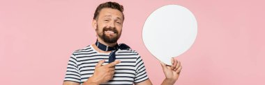 Çizgili tişört ve boyun atkısı giyen mutlu Fransız adam pembe pankartta izole edilmiş konuşma balonu tutuyor. 